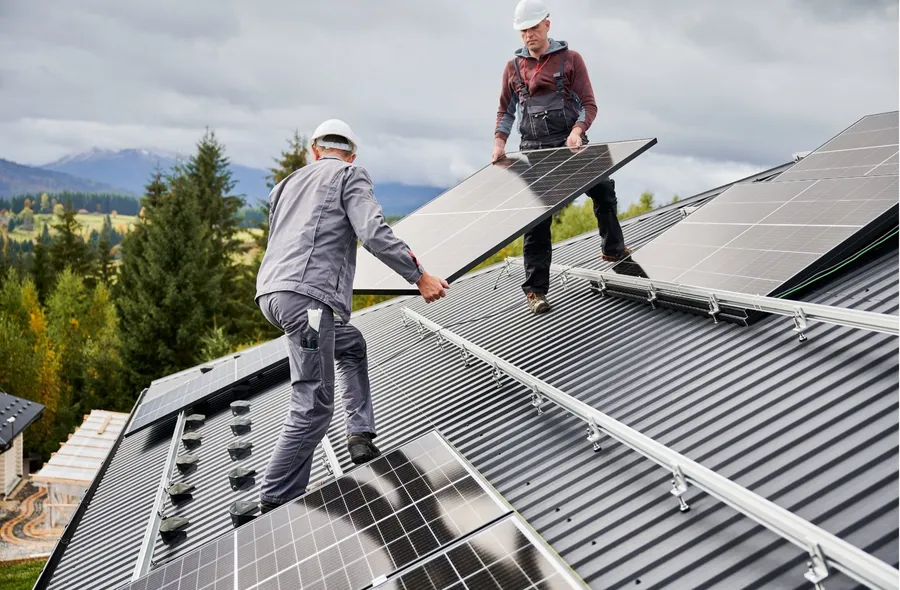Zwei Monteure tragen ein Solarmodul über ein Dach