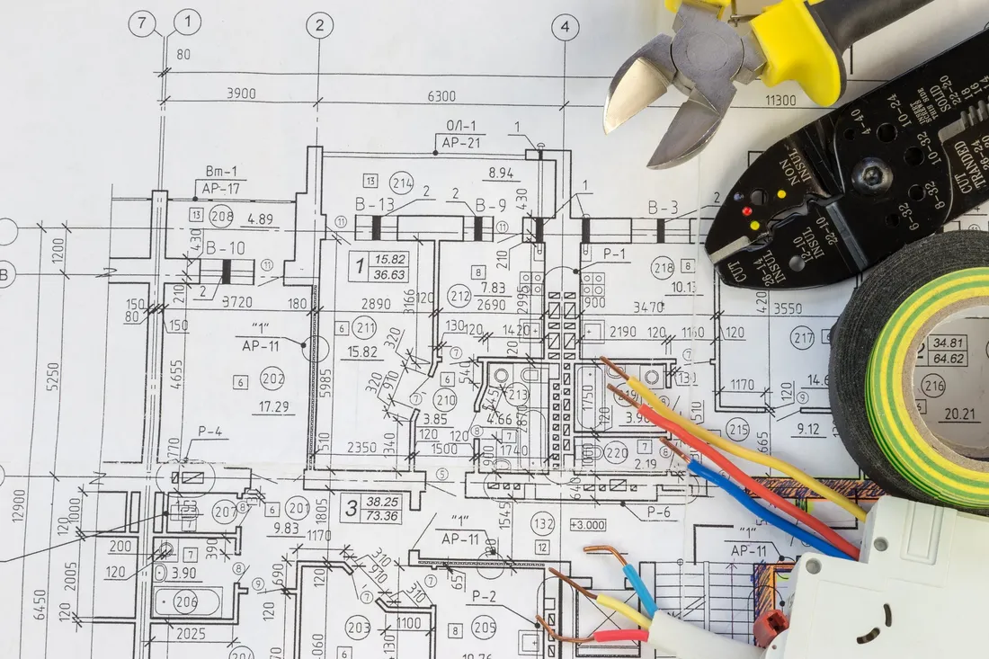 Elektroplan mit Abisolierzange, Kabeln und Isolierband auf dem Tisch